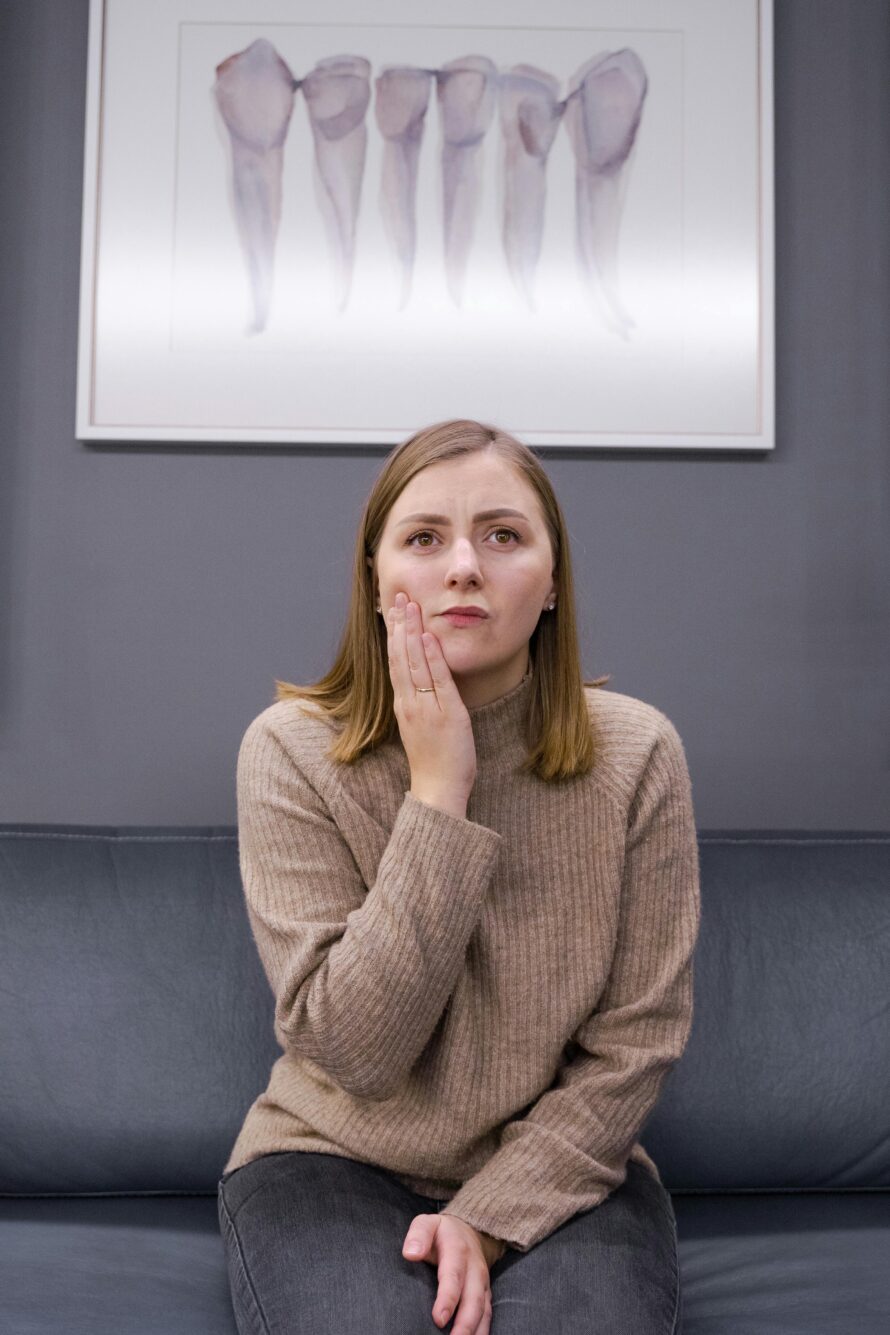 woman in pain touching her cheek sitting in dental office