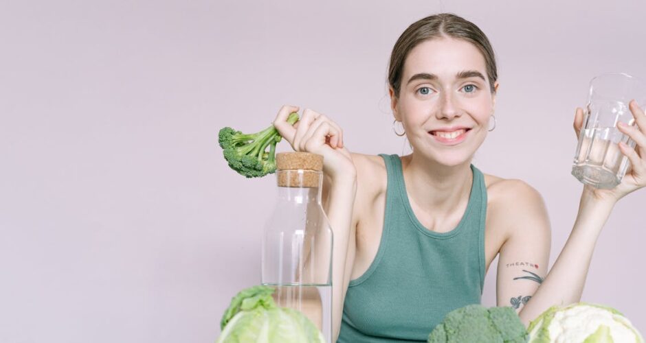 A woman in a green tank top holds a glass of water and a stalk of broccoli to illustrate Bellevue restaurant options that are good for your teeth.